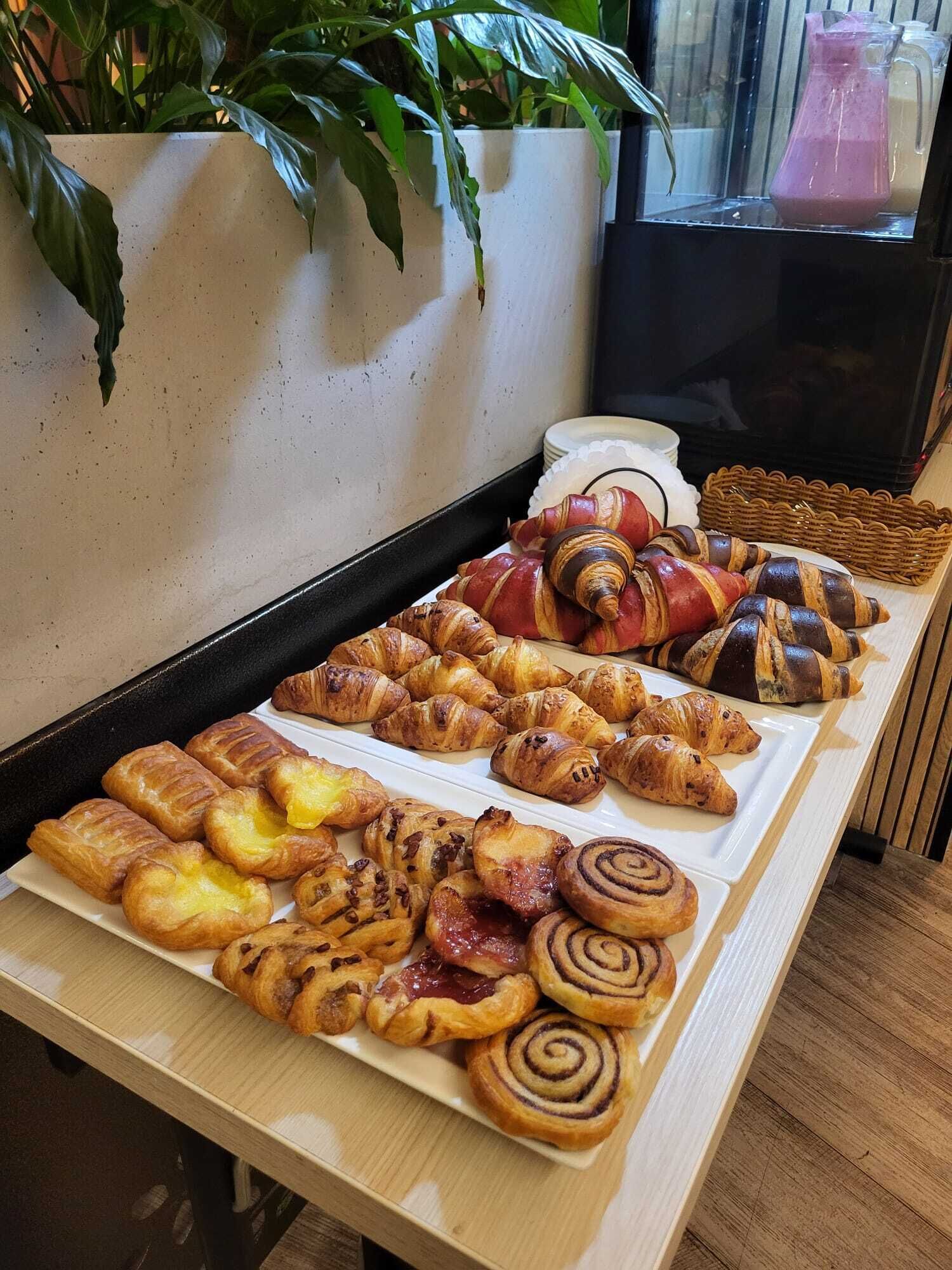 Una variedad de pasteles y pan en una bandeja, incluyendo croissants, rollos de canela y otras delicias horneadas.