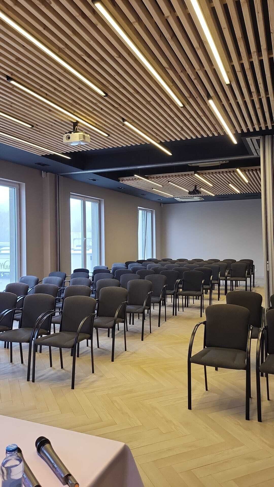 Ein Konferenzraum mit Reihen von Stühlen, einem Projektor und großen Fenstern.