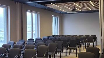 Ein Konferenzraum mit Reihen von Stühlen, einem Projektor und großen Fenstern.
