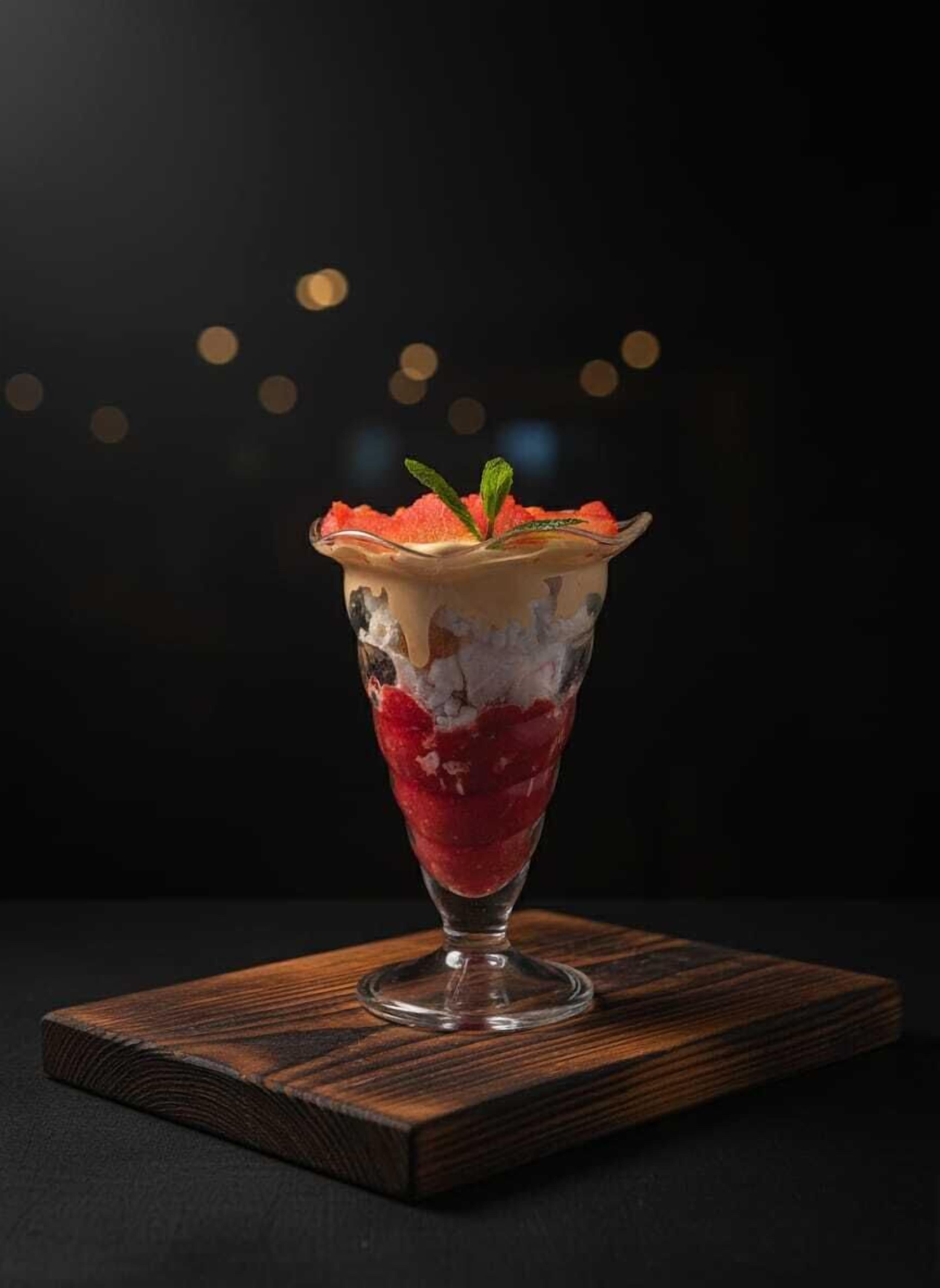 Un postre en capas dentro de un vaso alto sobre un posavasos de madera.