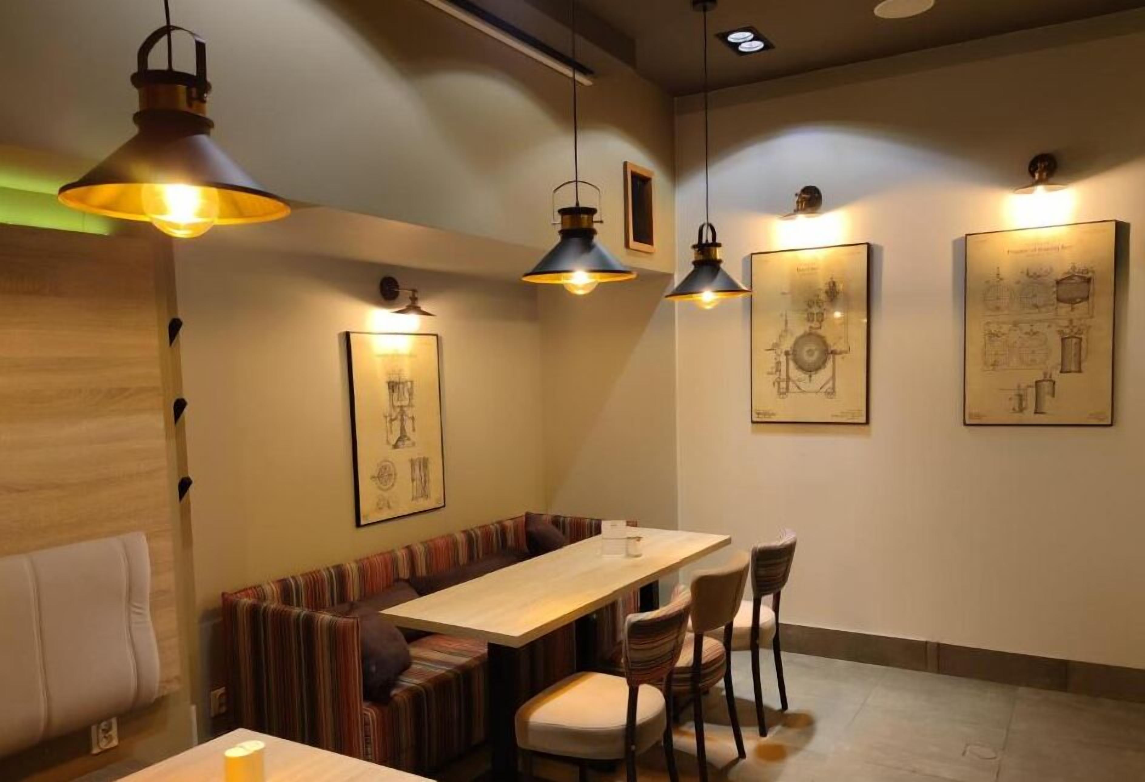 Interior de restaurante com uma longa mesa de madeira, assentos acolchoados listrados e iluminação pendente.