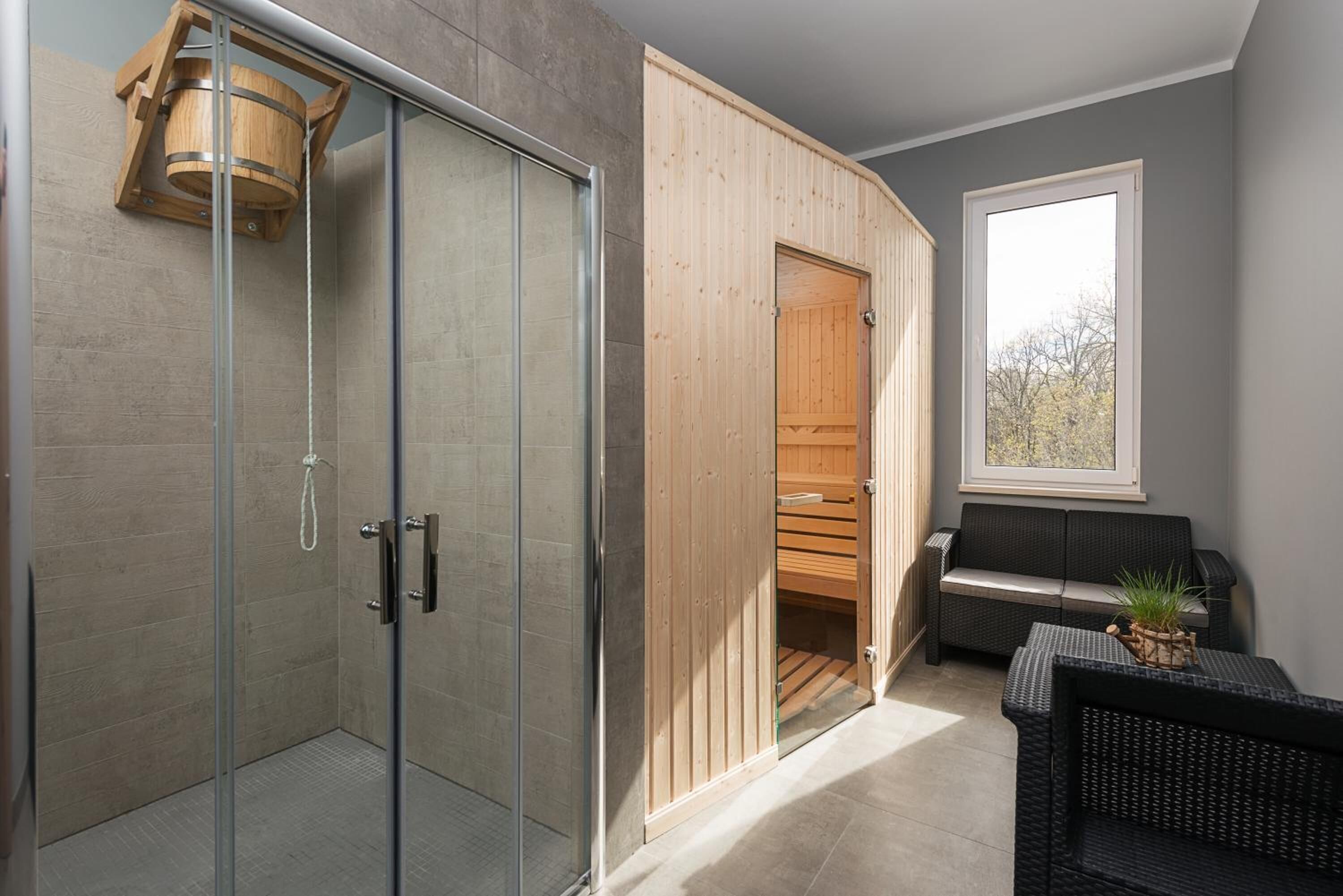 A modern bathroom with a glass shower enclosure, wooden door, and a bench with a potted plant.