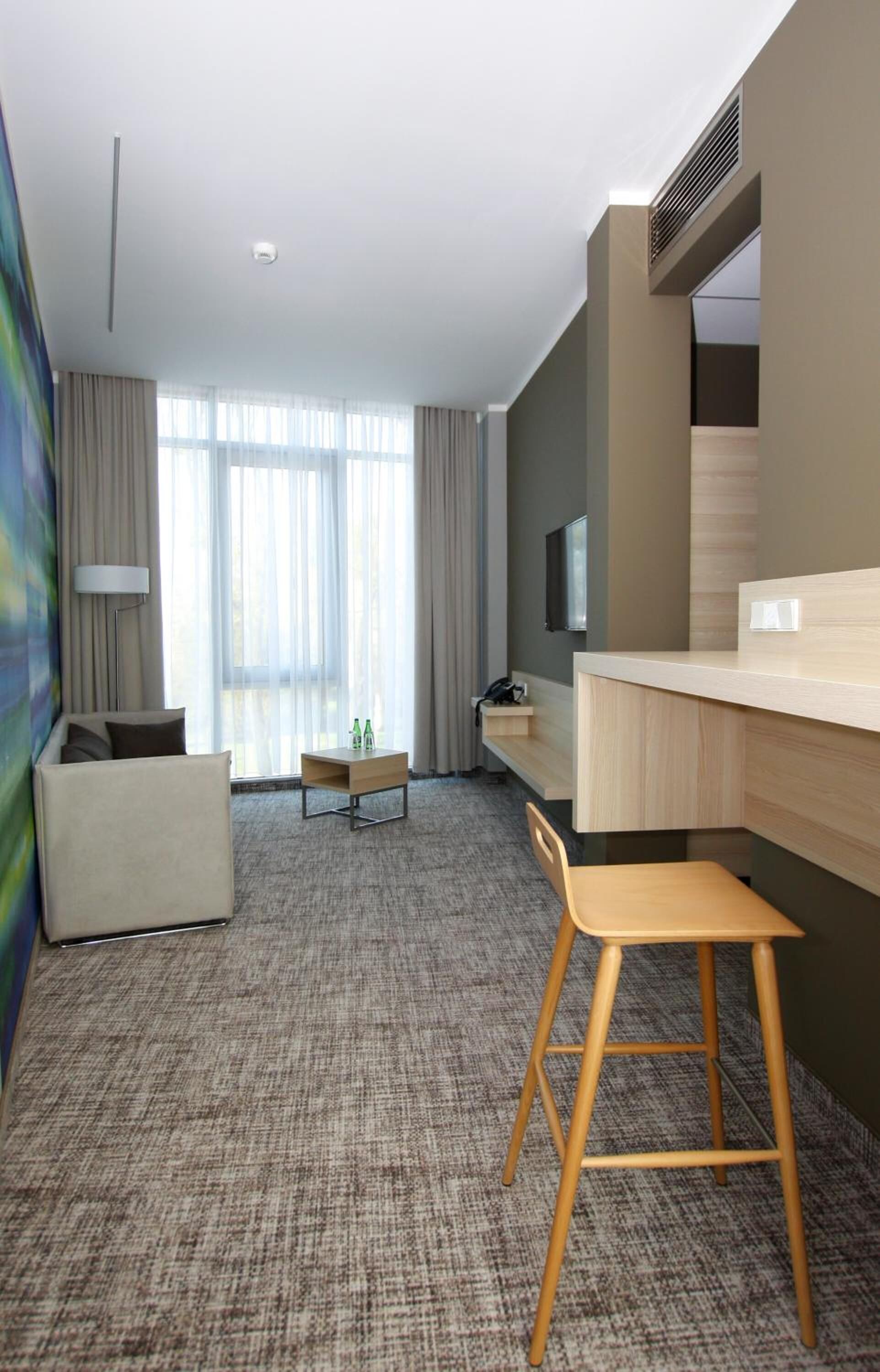 Et moderne hotelværelse med sofa, træstol, lille bord og tv ophængt på væggen.
