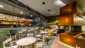 Eine moderne Bar mit verschiedenen Sitzgelegenheiten, darunter runde Tische und Stühle sowie eine Bar und eine Auswahl an Flaschen.