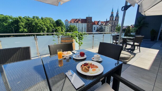 Ein Esstisch mit Frühstücksangeboten und Blick auf eine Stadtlandschaft mit historischen Gebäuden.