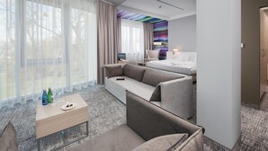 Ein modernes Hotelzimmer mit einem großen Bett, einer Couch, einem kleinen Tisch mit Getränken und Blick auf Bäume durch transparente Vorhänge.