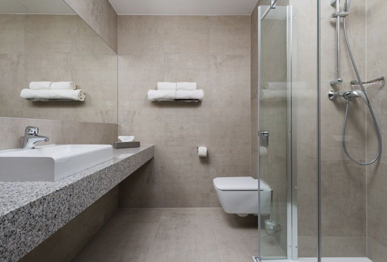 A modern bathroom with a granite countertop sink, a toilet, and a glass-enclosed shower area.
