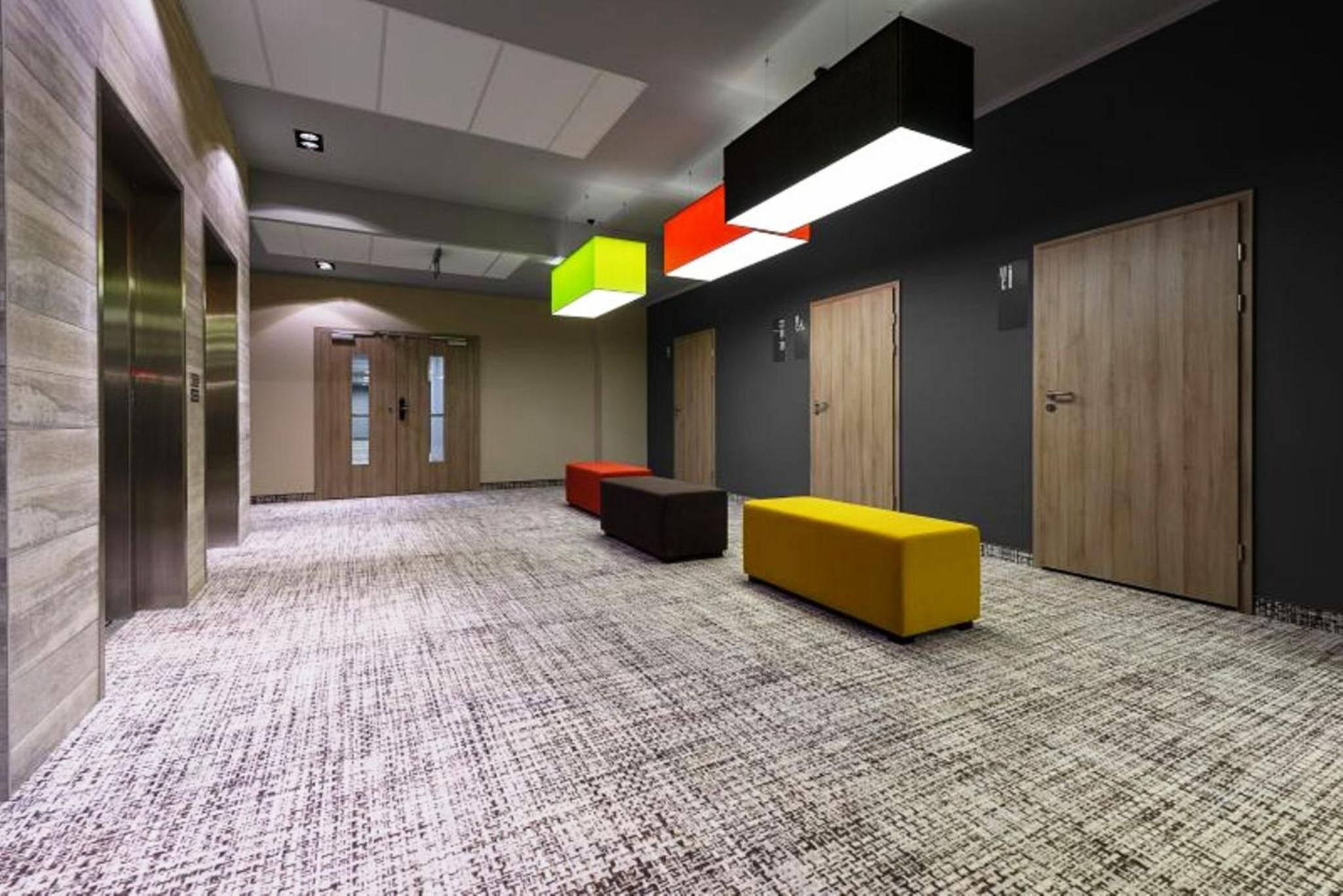 A hallway with a patterned carpet, wooden doors, and colorful geometric light fixtures.