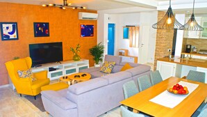 Ein modernes Wohnzimmer mit einer großen Couch, einem Fernseher und einem Essbereich mit Tisch und Stühlen.
