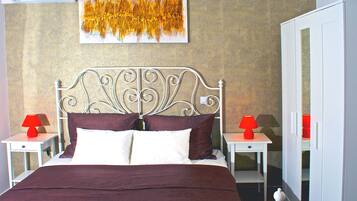 A neatly made bed with a metal headboard, two bedside tables with red lamps, and a large abstract painting on the wall.