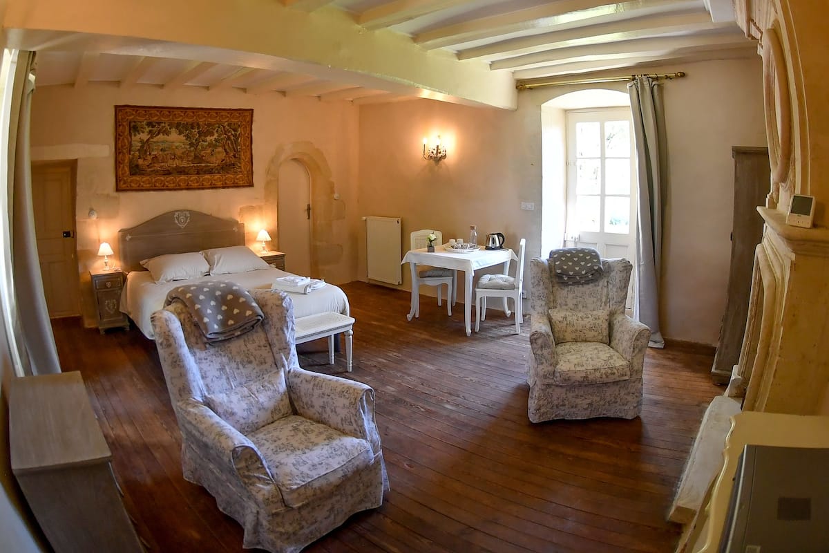 Una habitació acollidora amb un llit, dos seients còmodes, una taula petita i un quadre a la paret.