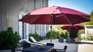 A patio area with outdoor seating, including a table and chairs, and two large red umbrellas providing shade. - Château de la Grand'Cour (Grandchamp-des-Fontaines)