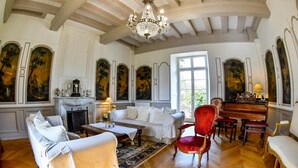 A spacious room with a grand chandelier, a piano, and classical paintings on the walls. - Château de la Grand'Cour (Grandchamp-des-Fontaines)