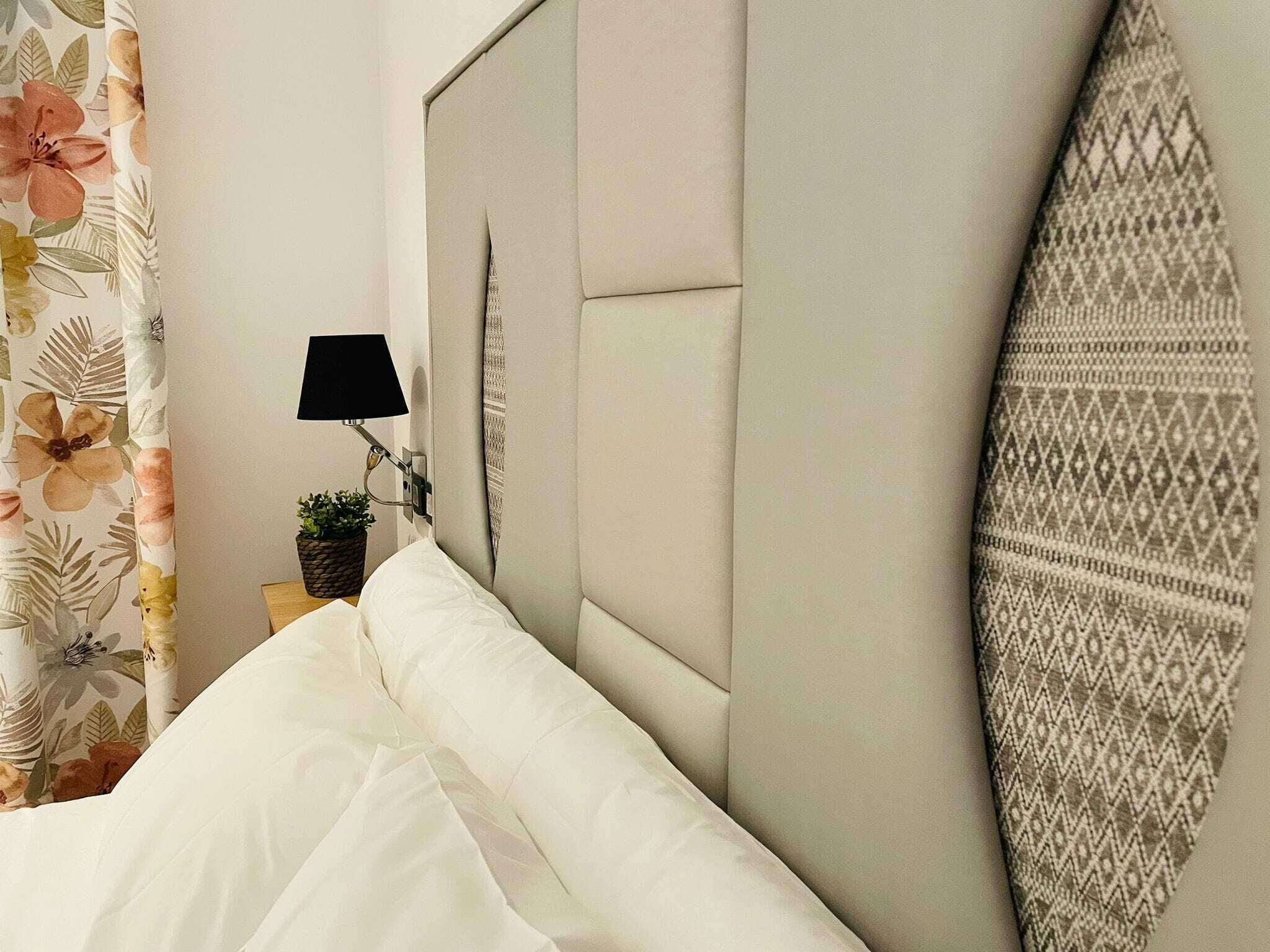 Camera da letto con un letto, una lampada a parete, una pianta in vaso e un elemento decorativo al muro.