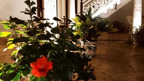 Una planta en maceta con una flor roja en una jardinera decorativa, una escalera con barandilla de hierro forjado y un suelo de baldosas.