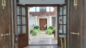 Una entrada de madera con puertas de vidrio que da a un patio con azulejos, plantas y otra puerta de madera al fondo.