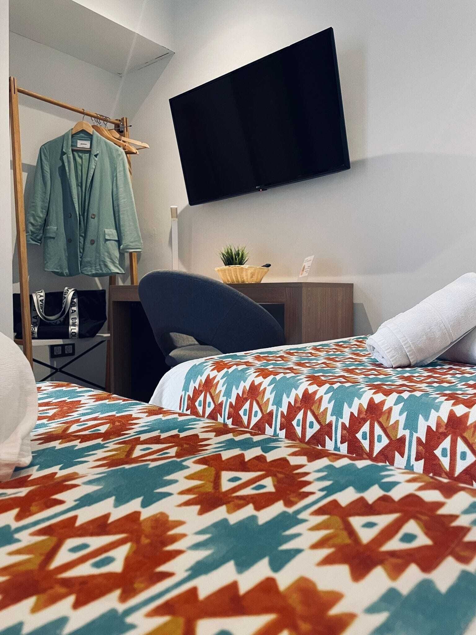 A hotel room with a bed, a desk, a chair, a TV, and a clothing rack.