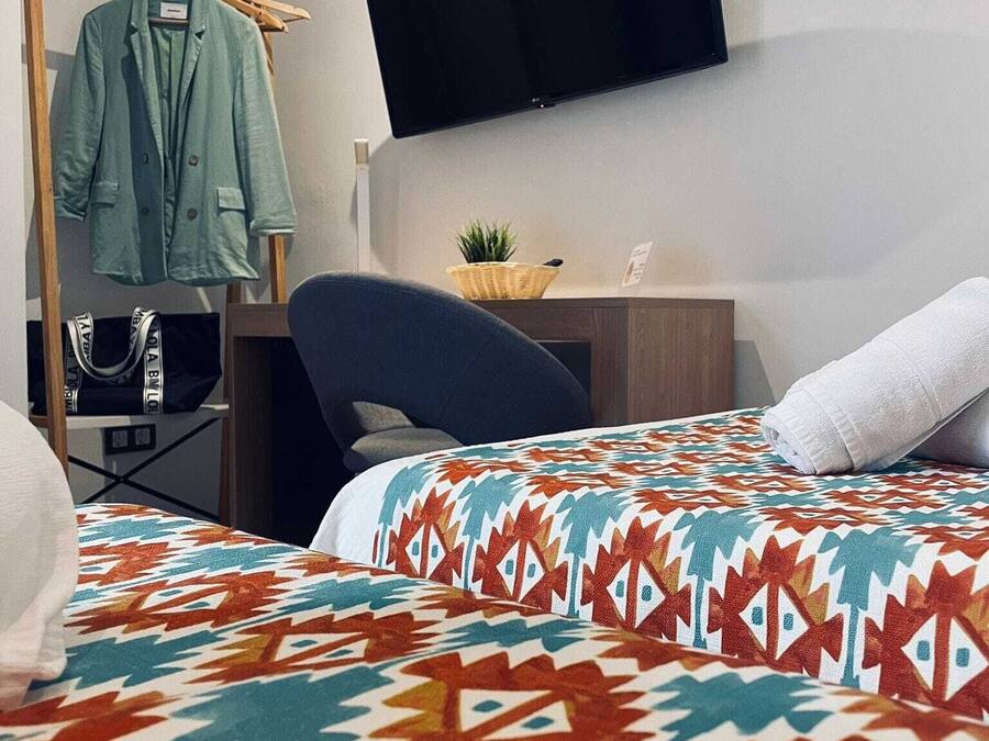 A hotel room with a bed, a desk, a chair, a TV, and a clothing rack.