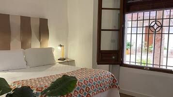 A bedroom with a bed, bedside lamp, window with bars, and a view of the outside.
