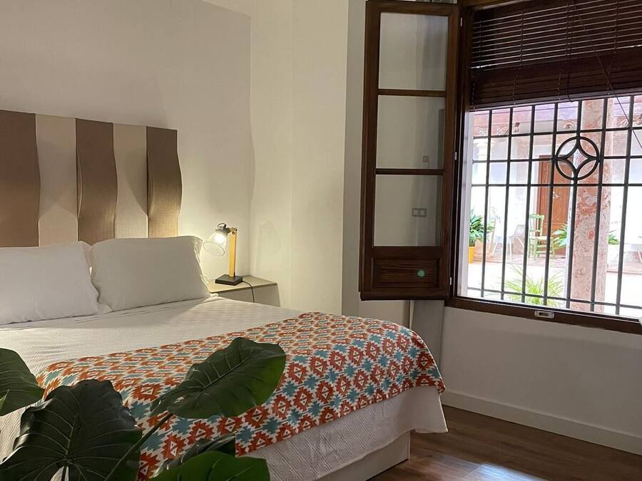 A bedroom with a bed, bedside lamp, window with bars, and a view of the outside.