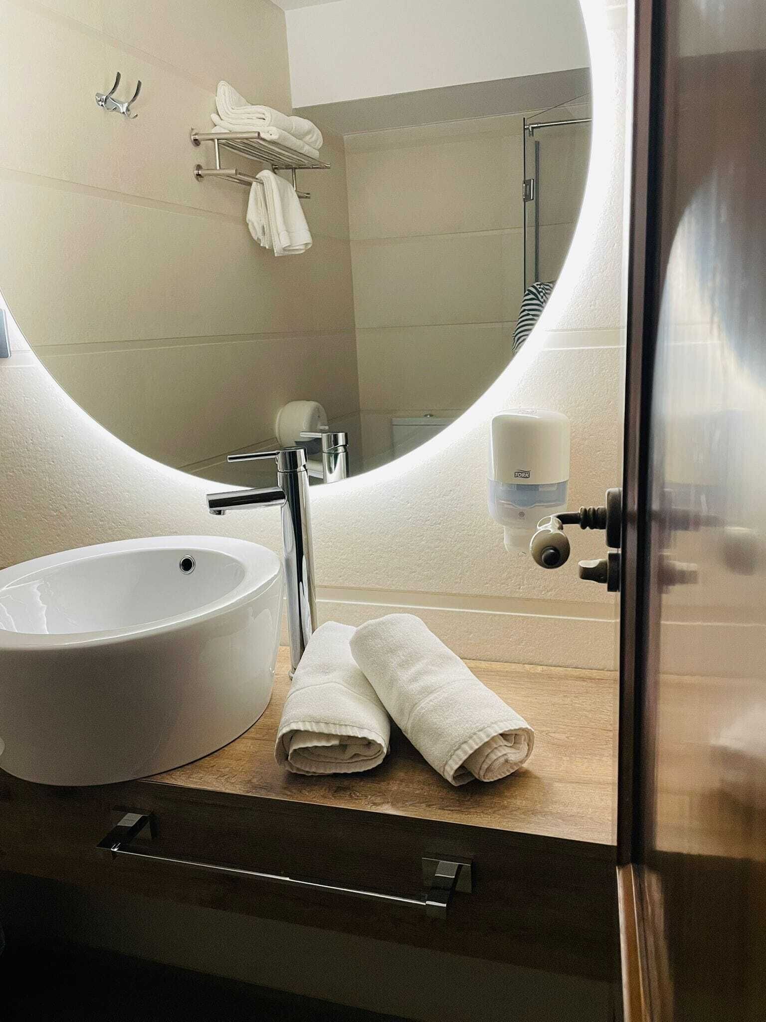 A modern bathroom with a large oval mirror, a white sink, and a towel rack.