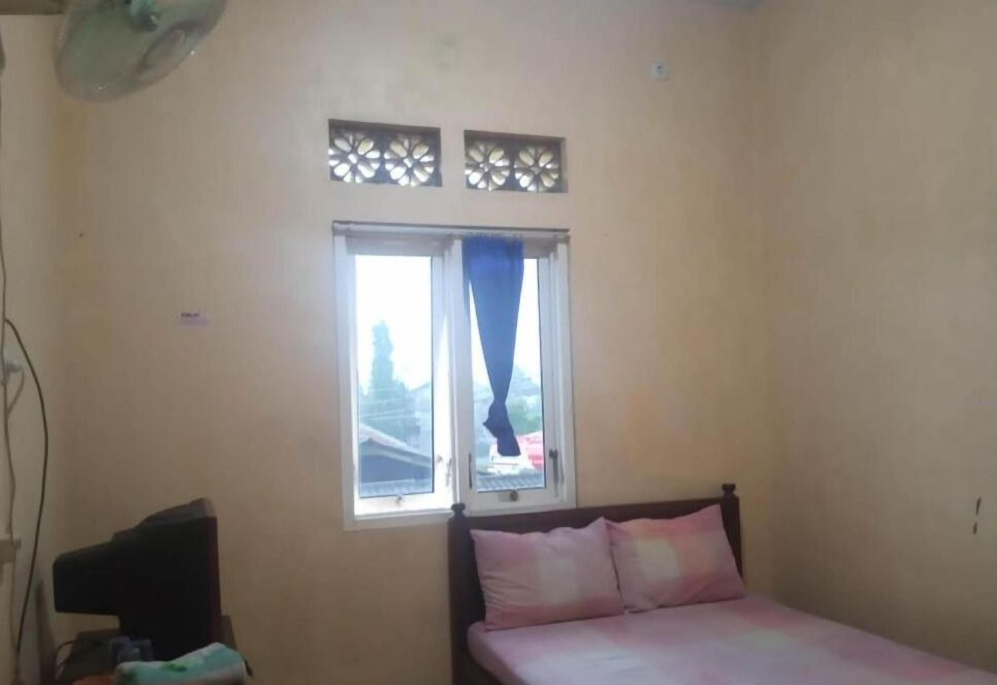 Une chambre à coucher avec un lit, une fenêtre avec des rideaux et un ventilateur fixé au mur.