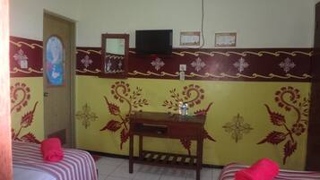 A room with two beds, a small table with a bottle, a TV on a stand, and decorative wall patterns.