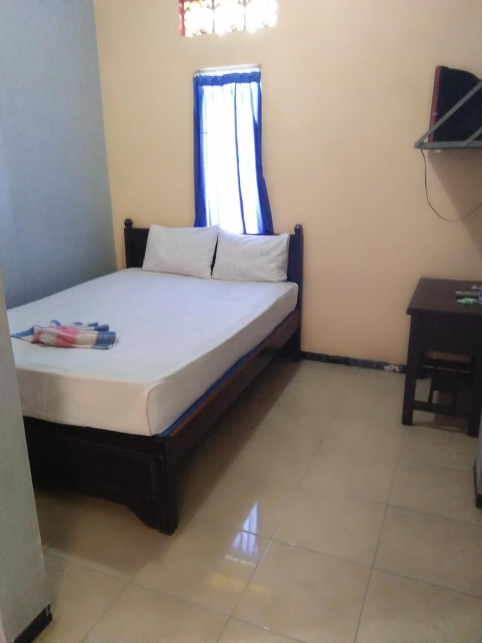 A single bed with a wooden frame, a bedside table, and a window with blue curtains.