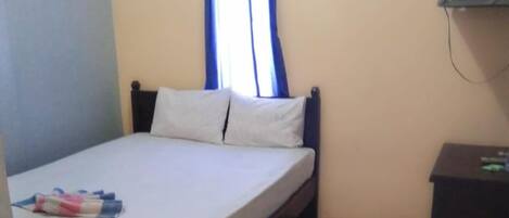 A single bed with a wooden frame, a bedside table, and a window with blue curtains.