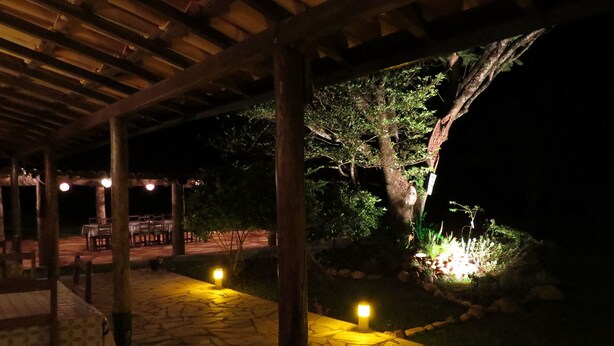 An outdoor patio area with stone flooring, wooden pergola, and tables and chairs under the shelter. - Praia da Crioula (Vargem Bonita)