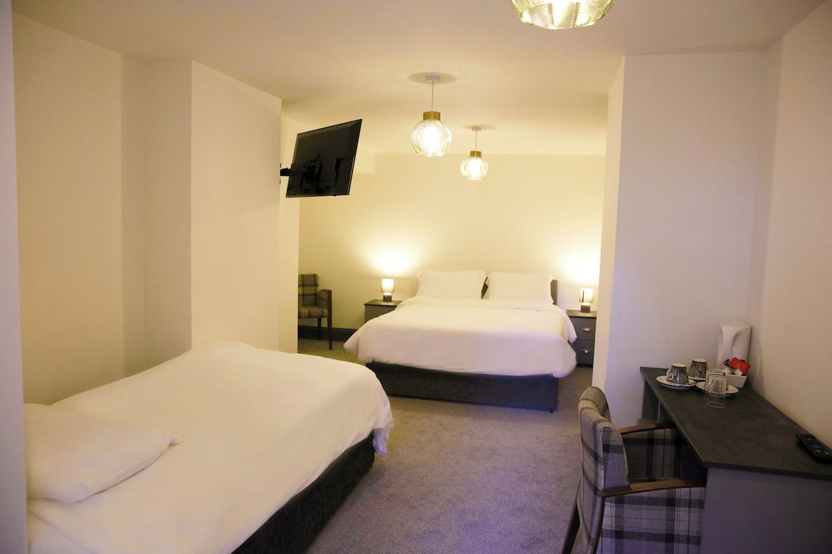 A hotel room with two beds, a desk with a chair, a TV mounted on the wall, and two pendant lights.