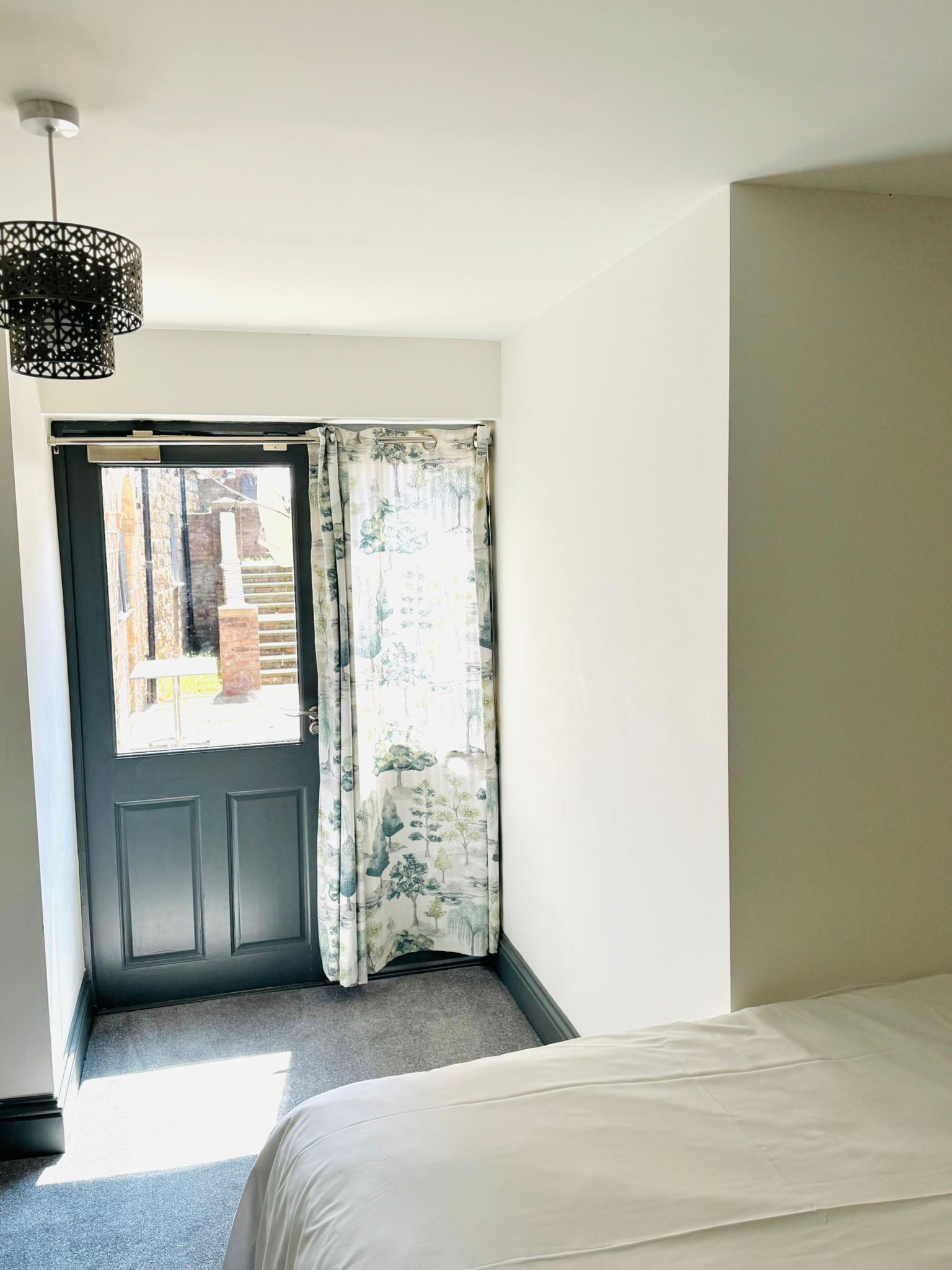 Een slaapkamer met een bed, een deur met gordijn en een hanglamp.