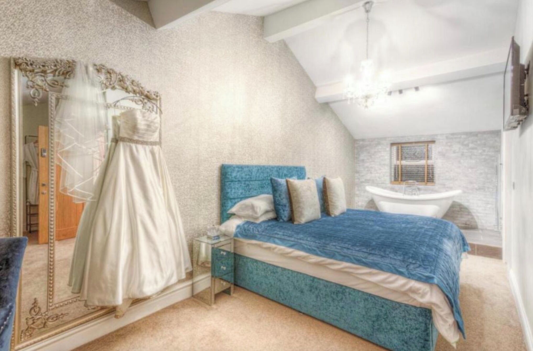 Une chambre avec un grand lit, une coiffeuse avec un miroir et une robe posée sur le sol.