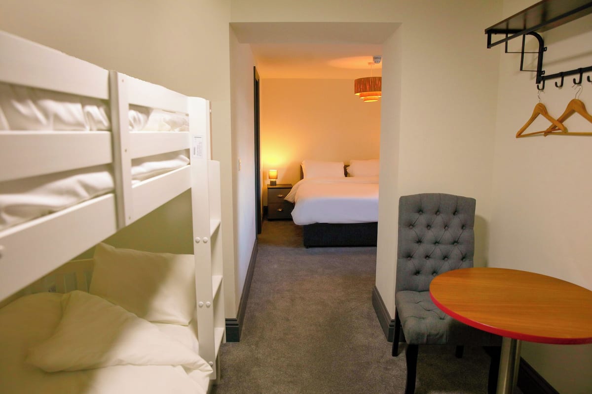 A hotel room with bunk beds, a single bed, a tufted armchair, and a small table.