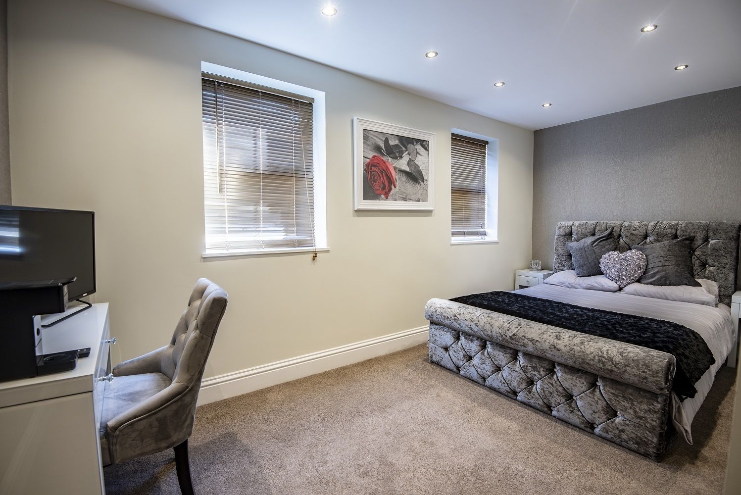 A bedroom with a bed, a desk, a chair, and two windows with blinds.