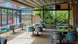 An outdoor dining area with tables and chairs, large windows, and a view of greenery. - George Wright Boutique Hotel, Bar & Restaurant. (Rotherham)