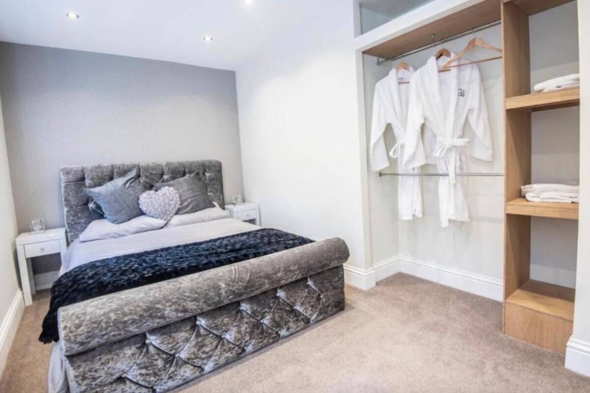 A bedroom with a bed, a bedside table, a nightstand, a wardrobe, and a closet with hanging robes.