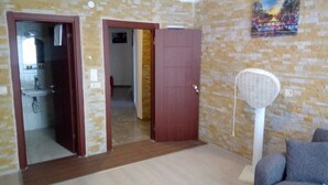 Una habitación con pared de piedra, una puerta que da a otra habitación, un ventilador blanco y un sofá gris.