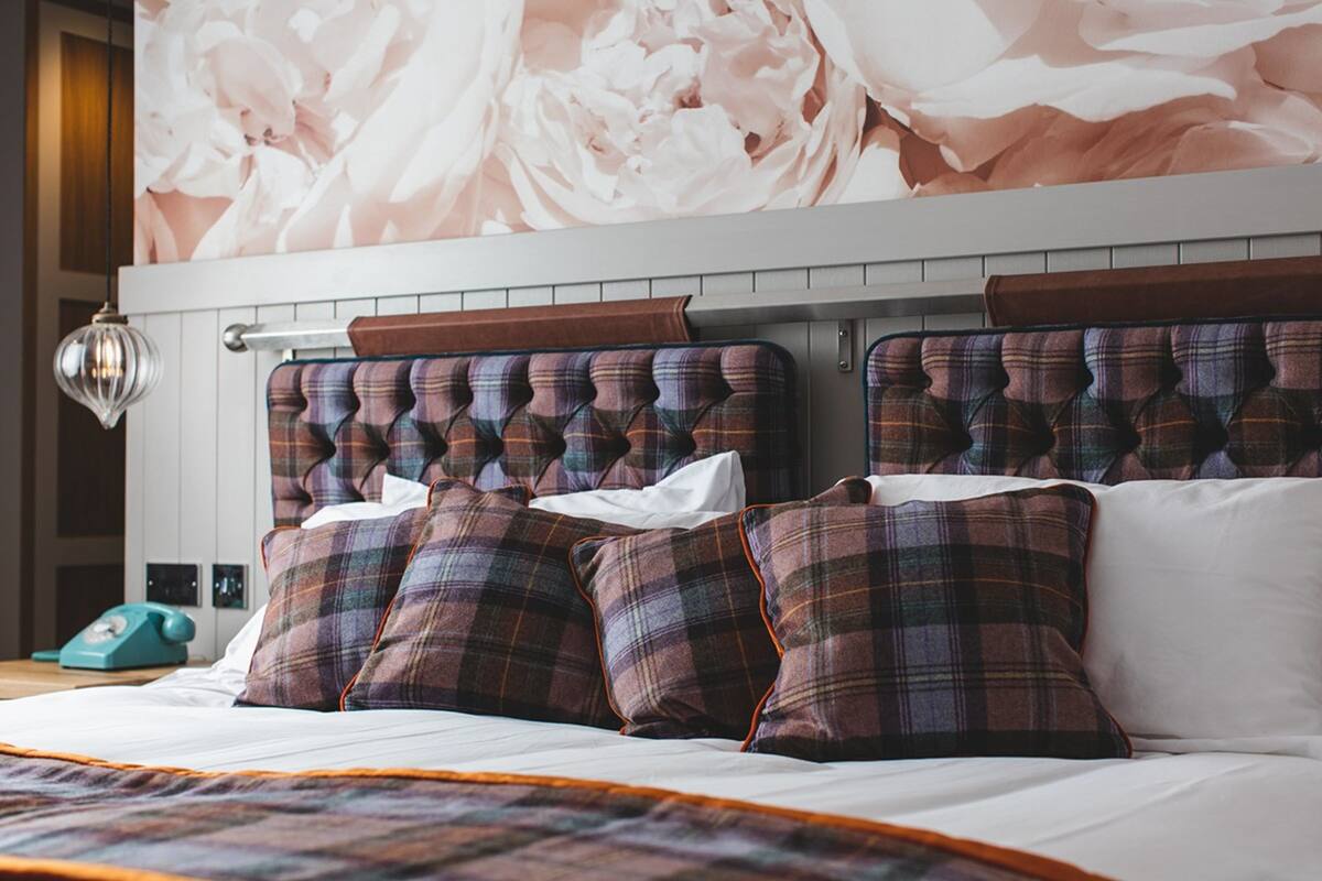Cama bem arrumada com almofadas xadrez e cabeceira com design acolchoado.