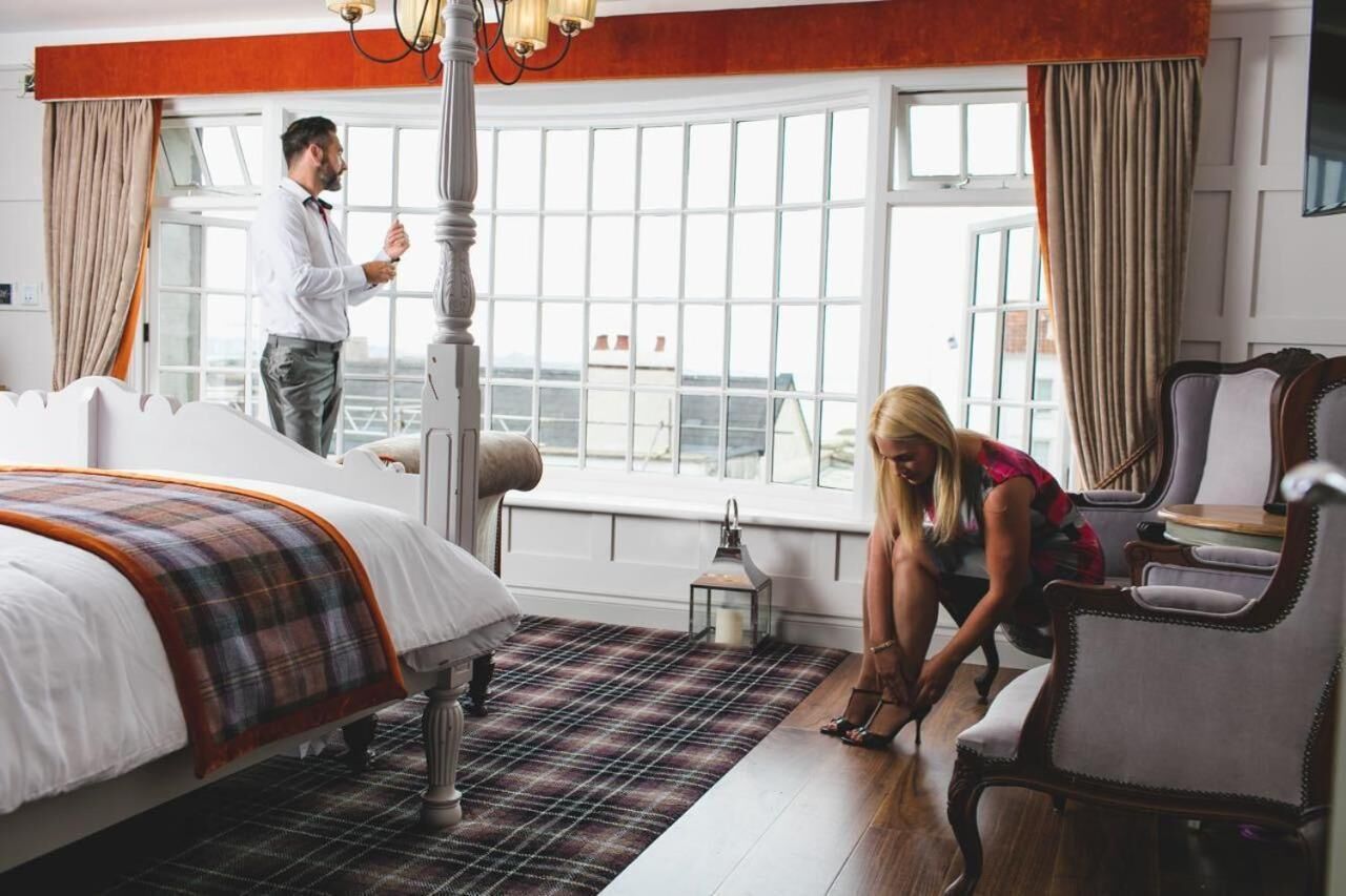 A hotel room with a large bed, a window with curtains, a chair, and a lamp.