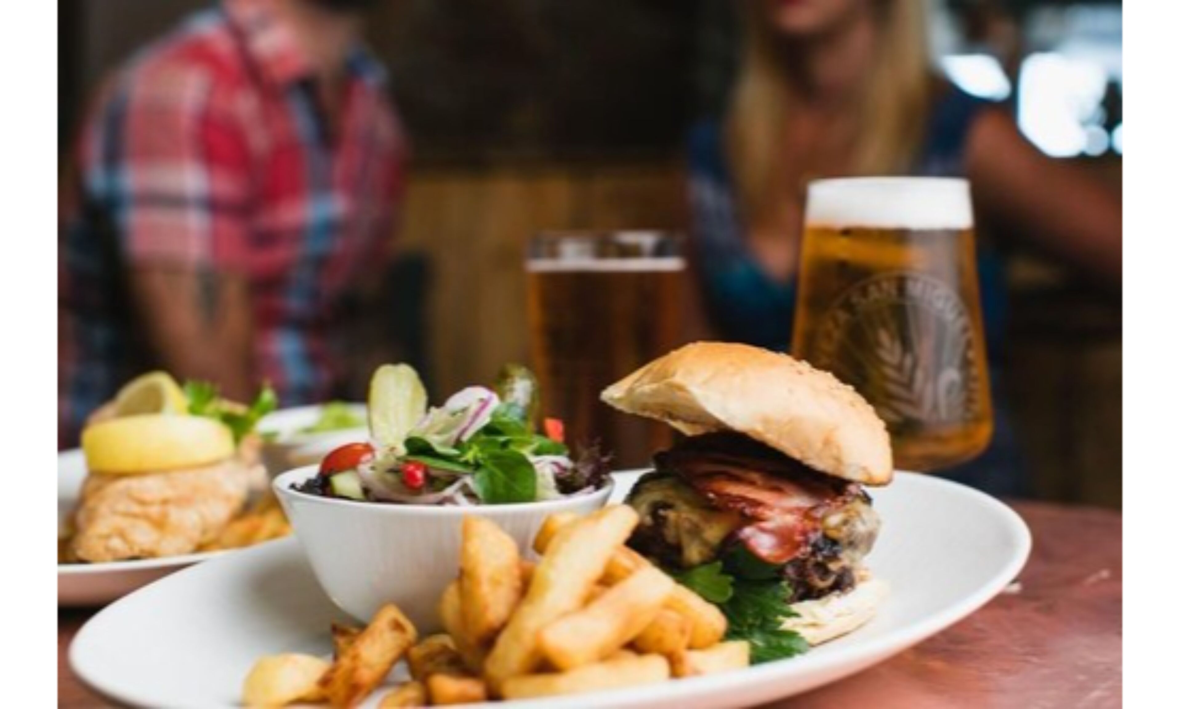 A meal consisting of a burger, fries, and a salad on a plate, with a beer glass in the background.