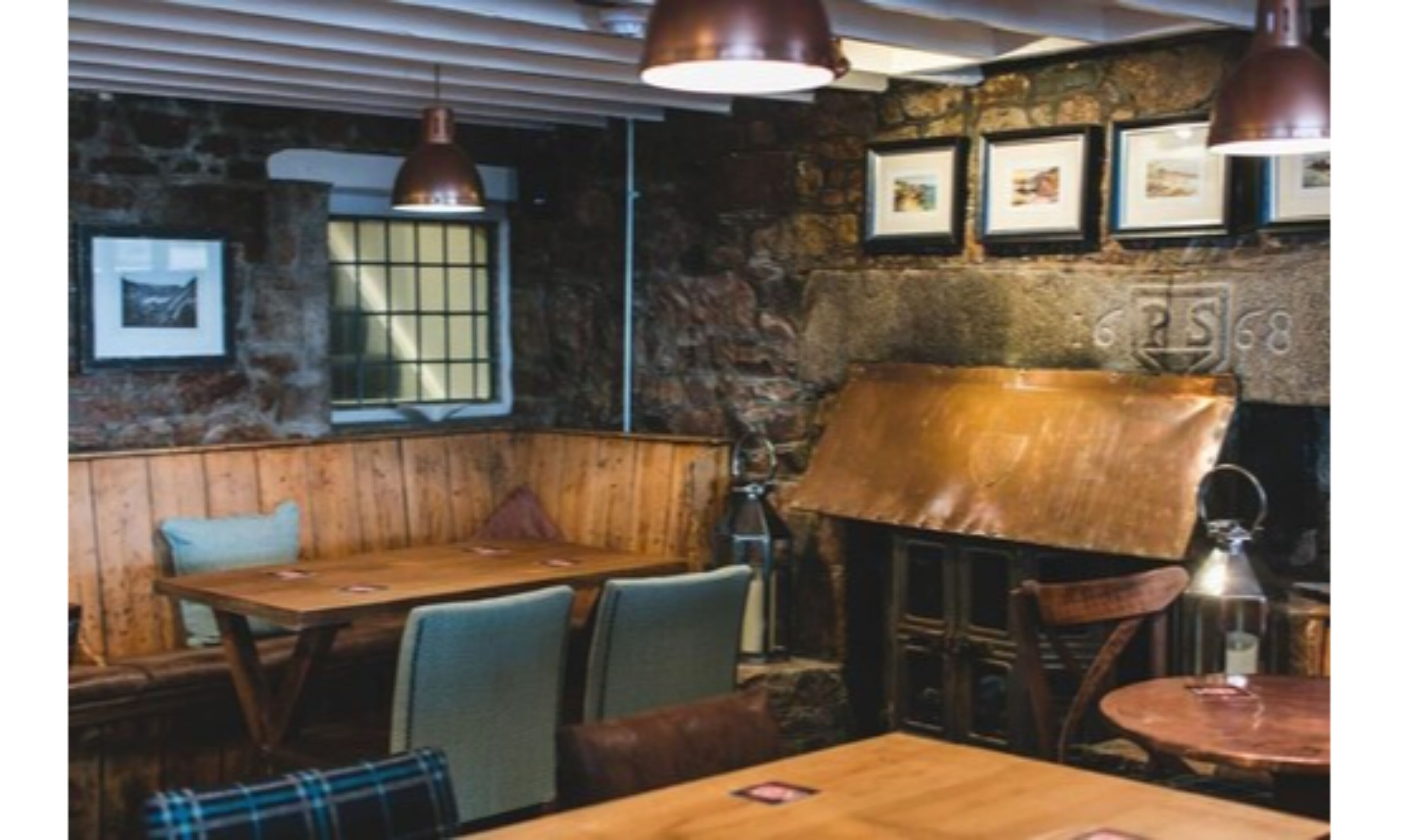 Un intérieur rustique avec des tables et des bancs en bois, des murs en pierre et des tableaux encadrés accrochés au mur.