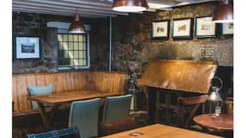 Un intérieur rustique avec des tables et des bancs en bois, des murs en pierre et des tableaux encadrés accrochés au mur.