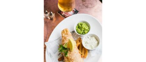 A plate with fish and chips, a glass of beer, and two side dishes.