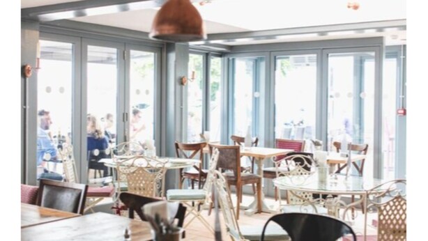 A restaurant interior with multiple tables and chairs, large windows, and hanging pendant lights. - The Old Courthouse Inn (St. Brelade)