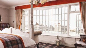 A room with a large bed, a window with a city view, a chandelier, and a plaid-patterned rug. - The Old Courthouse Inn (St. Brelade)