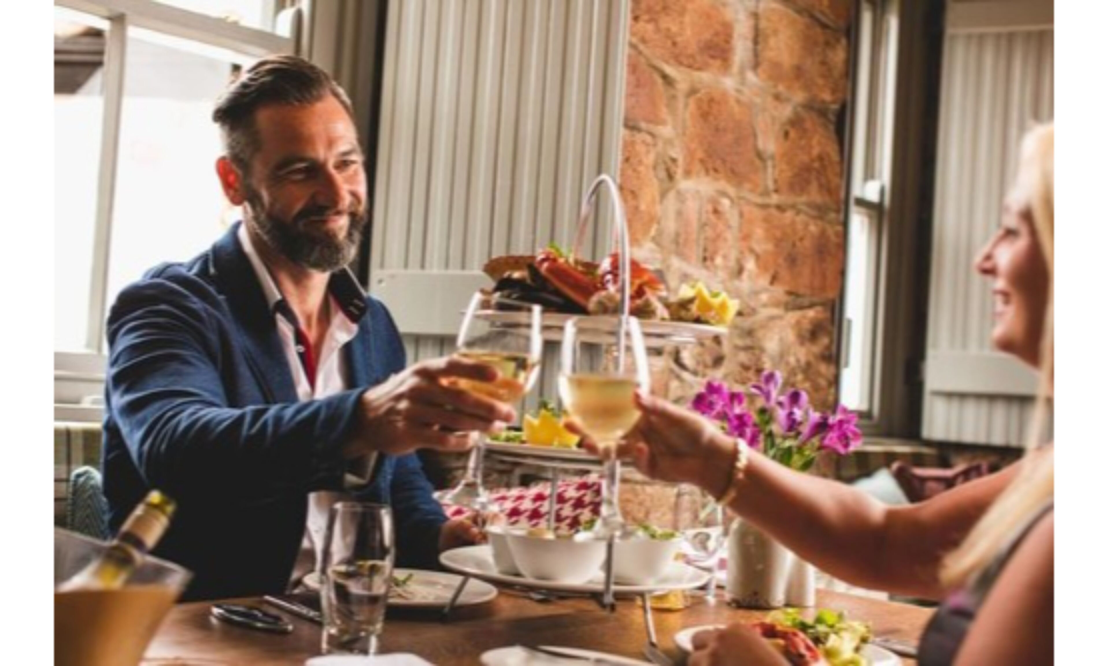 Una mesa de comedor con un dispensador de bebidas de tres niveles, platos de comida y una botella de vino.