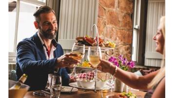 Una mesa de comedor con un dispensador de bebidas de tres niveles, platos de comida y una botella de vino.