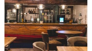 A bar area with wooden counter, multiple bottles, and a television screen. - The Old Courthouse Inn (St. Brelade)