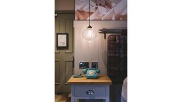 A vintage-style telephone on a wooden table with a drawer below, a wall-mounted light fixture, and a framed picture above.